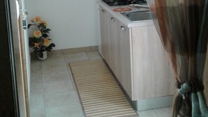 Una cocina compacta con estufa a gas, un fregadero y un ventanal con cortina. Hay una planta en maceta y un felpudo en el suelo.