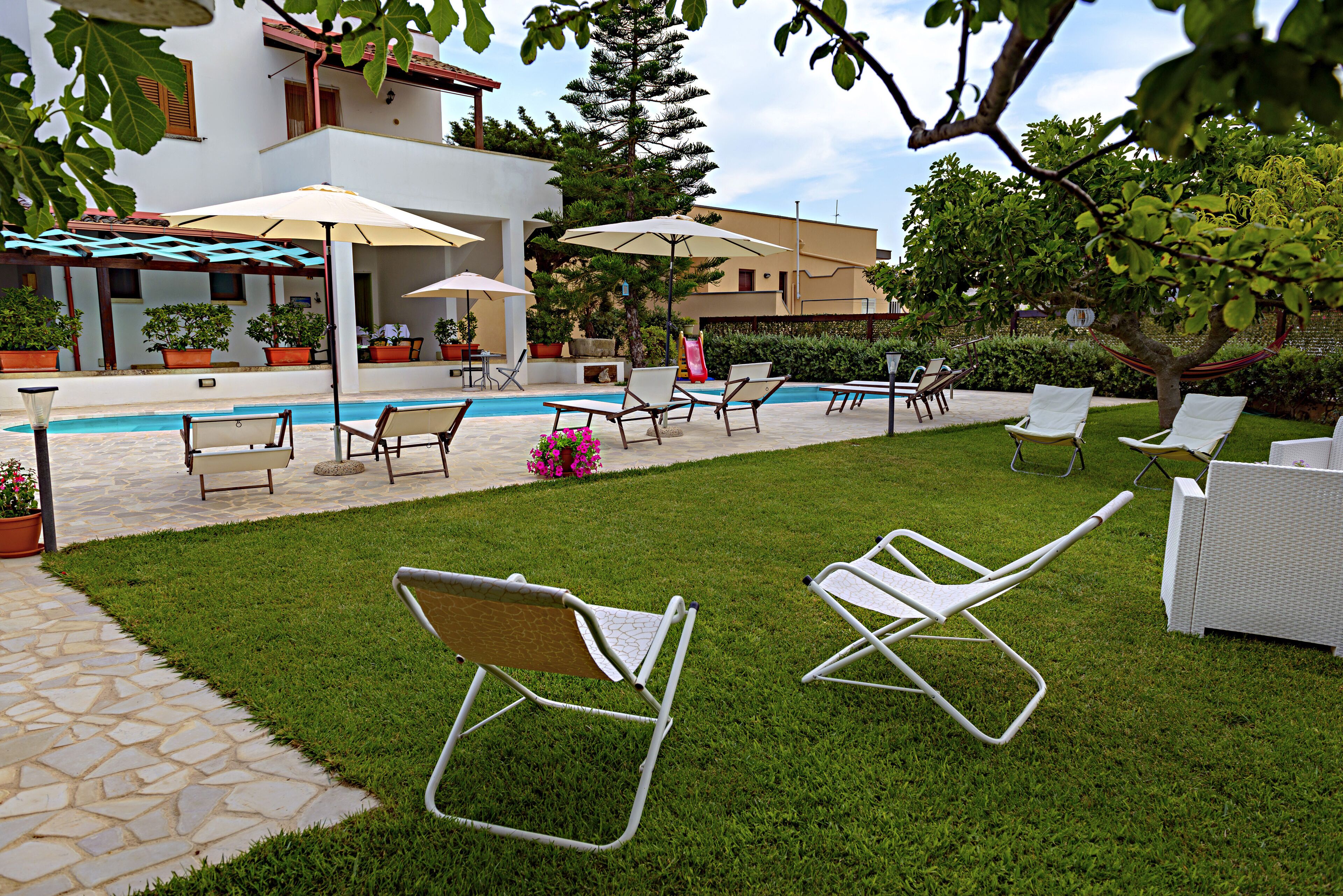 A poolside area with lounge chairs, umbrellas, and potted plants.