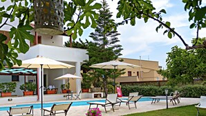 Un área junto a la piscina con sillones de descanso, sombrillas y un pequeño jardín.