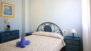A bedroom with a bed, a nightstand, a lamp, a dresser, and a framed picture on the wall.