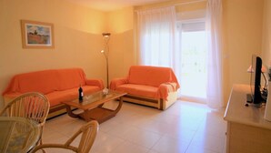 A living room with two orange sofas, a glass coffee table, a floor lamp, a TV on a stand, and a painting on the wall.