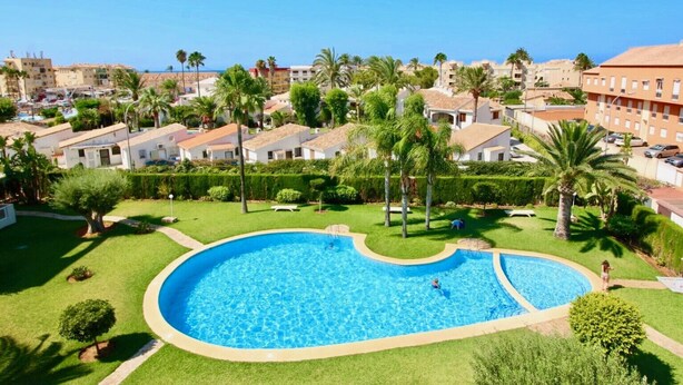 A swimming pool surrounded by well-maintained lawns and palm trees, with buildings in the background.