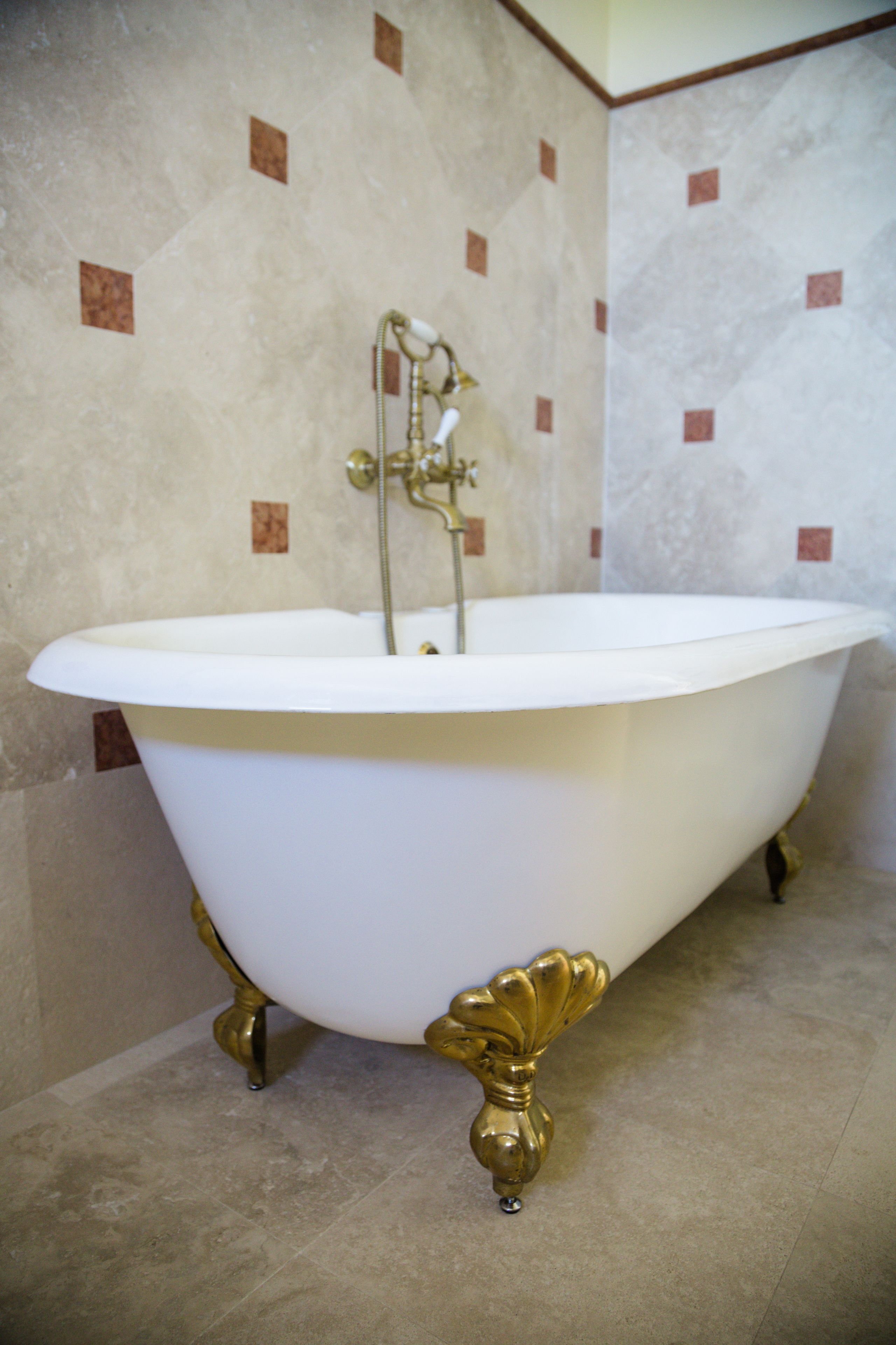 A freestanding bathtub with ornate gold fixtures, set against a tiled wall with a repeating pattern.