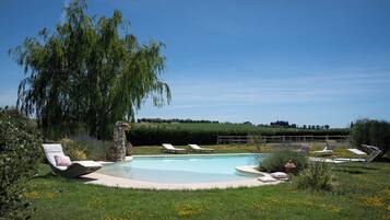 Une piscine ronde entourée de chaises longues, avec un arbre au centre.