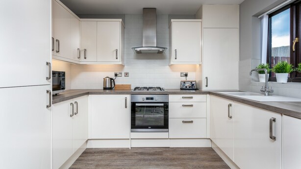 A modern kitchen with white cabinets, stainless steel appliances, and a window with plants. - The Huntington - Donnini Apartments (Ayr)