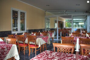A restaurant with wooden chairs and tables, covered with patterned tablecloths. - Hotel Garda (Darmstadt)