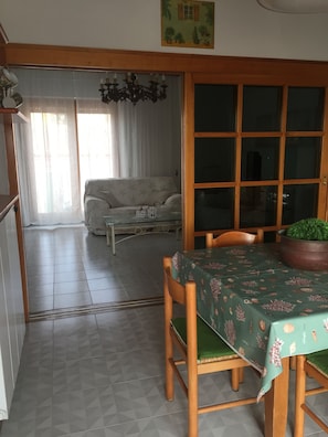 En matplats med ett bord dukat för två personer, en soffa i bakgrunden och ett stort fönster med gardiner.