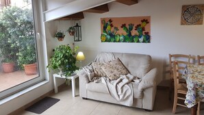 A cozy living room with a sofa, a coffee table, and a dining table with chairs. There is a window with a view of greenery outside. - PalermiT'Amo Apartment (Palermo)