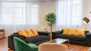 Una sala de estar con dos sofás oscuros, un sillón verde y una mesa de centro de vidrio.