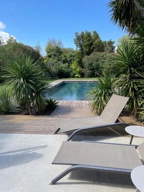 A poolside area with lounge chairs and a table, surrounded by greenery. - Guesthouse Le Mas de la Dame (Saint-Tropez)