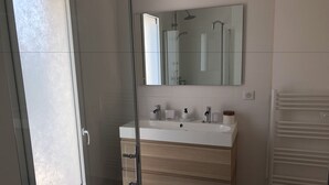 A modern bathroom with a large mirror, a white sink, and a glass shower enclosure. - Guesthouse Le Mas de la Dame (Saint-Tropez)