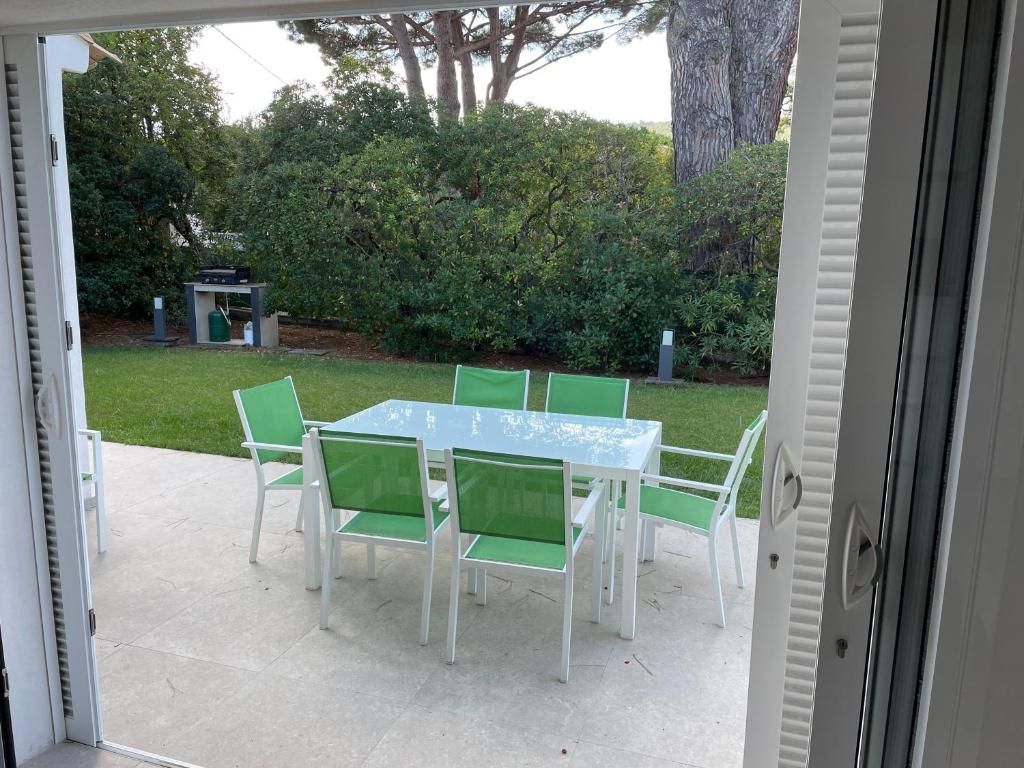 En udendørs terrasse med et bord, stole, grill og en hæk i baggrunden.