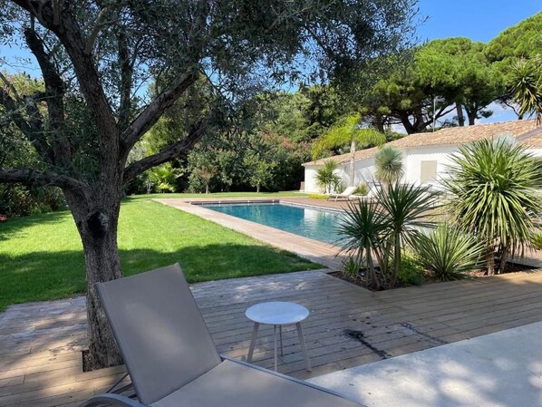 Un área junto a la piscina con terraza de madera, una silla de descanso y una pequeña mesa.