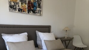 A neatly made bed with a quilted cover, a grey upholstered headboard, and a wall-mounted artwork above it. - Guesthouse Le Mas de la Dame (Saint-Tropez)