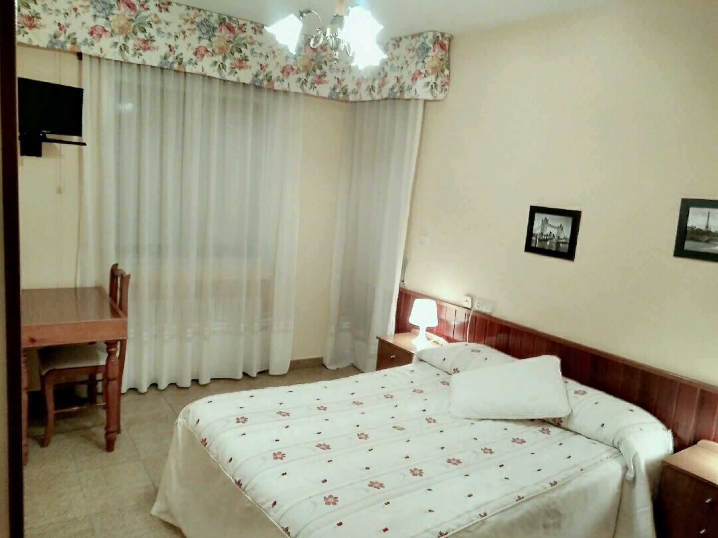 A hotel room with a bed, a desk, a chair, a nightstand, and a lamp.
