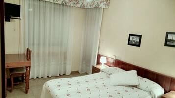 A hotel room with a bed, a desk, a chair, a nightstand, and a lamp.