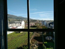 Vista a través de una ventana de una zona residencial con edificios, un viñedo y una montaña al fondo.