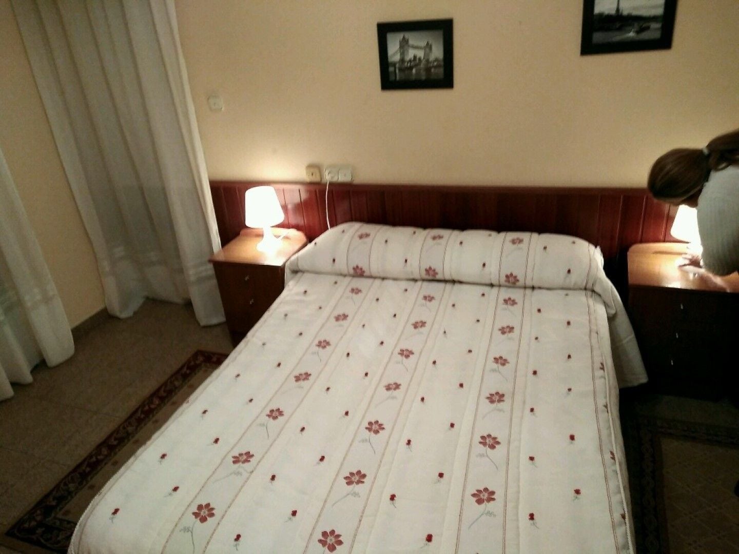 Une chambre d’hôtel avec un lit, deux tables de chevet, une commode, une lampe, un tableau au mur et une fenêtre avec des rideaux.