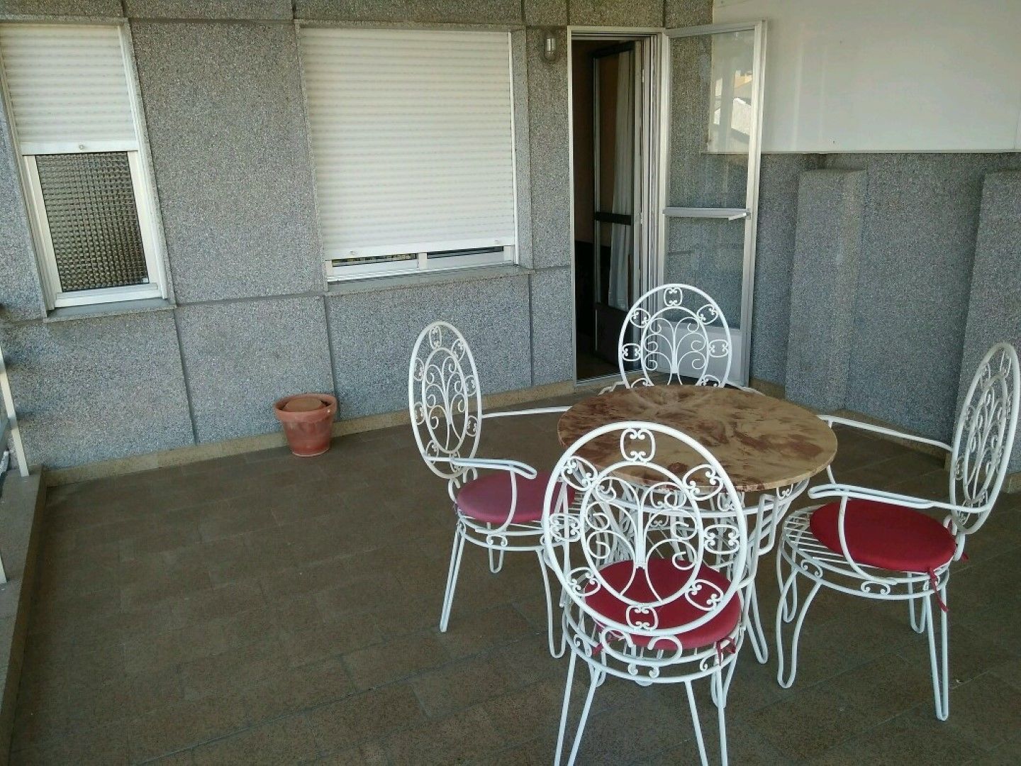 A patio with a round table and four white metal chairs with red cushions.
