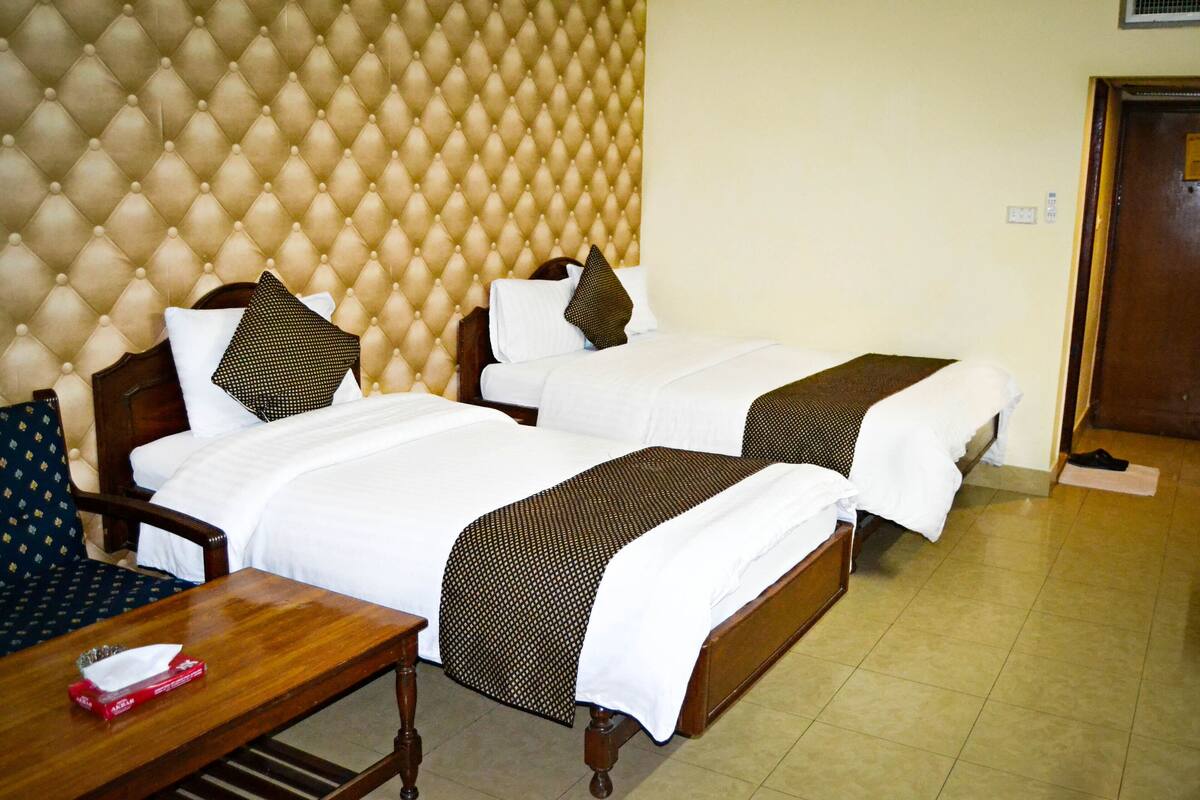 A hotel room with two beds, a wooden nightstand, and a cushioned headboard.