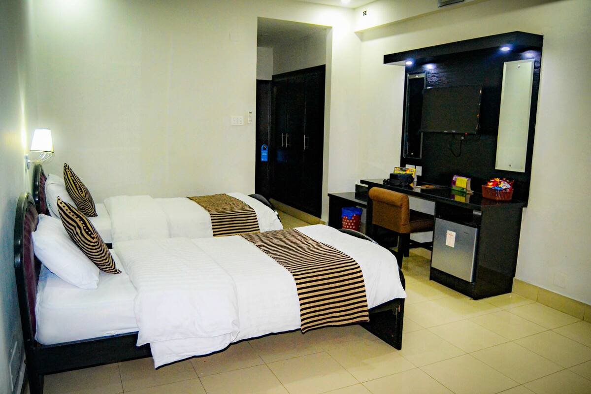 A hotel room with two beds, a desk with a mirror, and a small kitchenette.