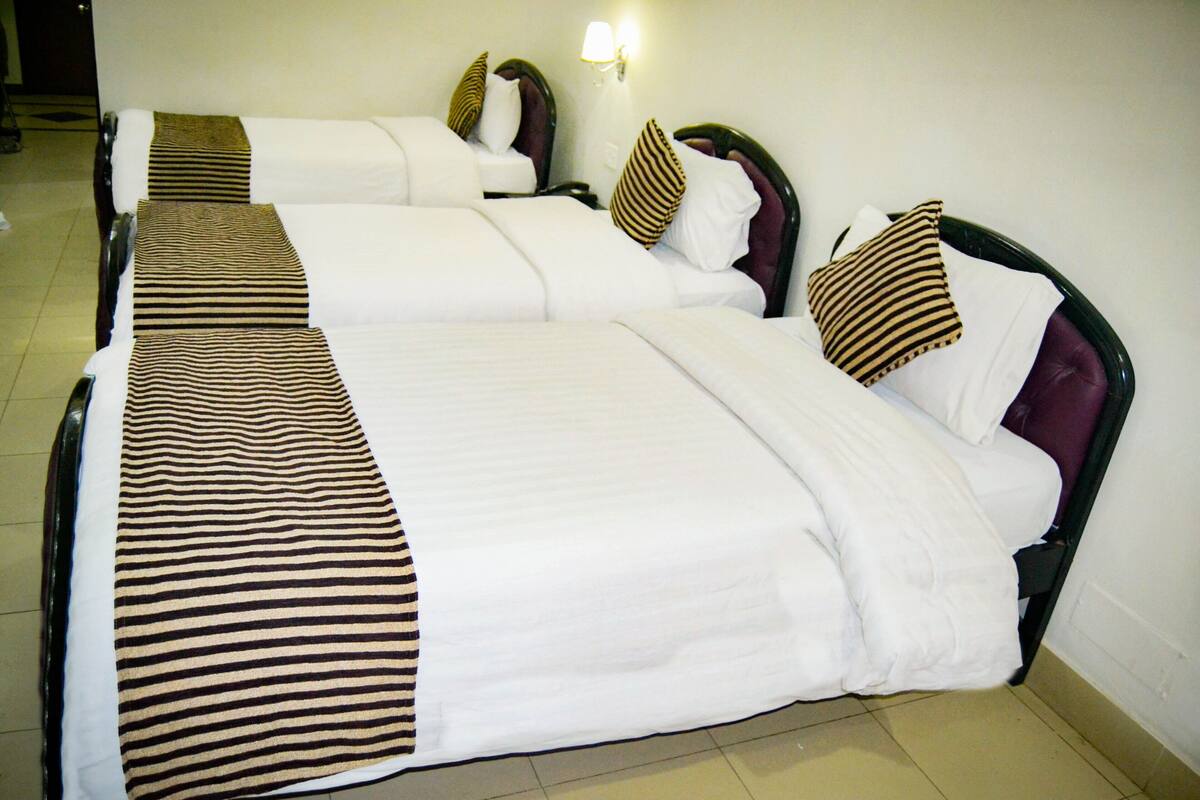 A hotel room with three beds, each with a striped blanket and matching pillows.
