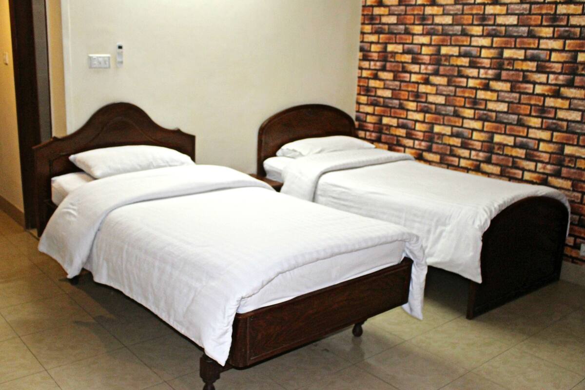 A room with two wooden beds, white bedding, a brick-patterned wall, and a tiled floor.