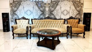 A seating area with three upholstered chairs and a glass-top coffee table, set against a marble-patterned wall. - Hotel Akbar International (Rawalpindi)