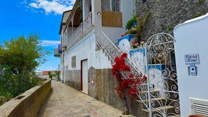 A narrow street with a white building featuring a balcony and a metal gate. - Casa Mimì in Moressa area (Praiano)
