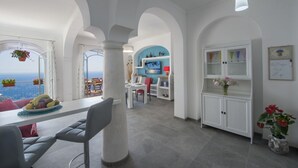 A modern interior with a dining area, white cabinets, and a view of the sea. - Casa Mimì in Moressa area (Praiano)