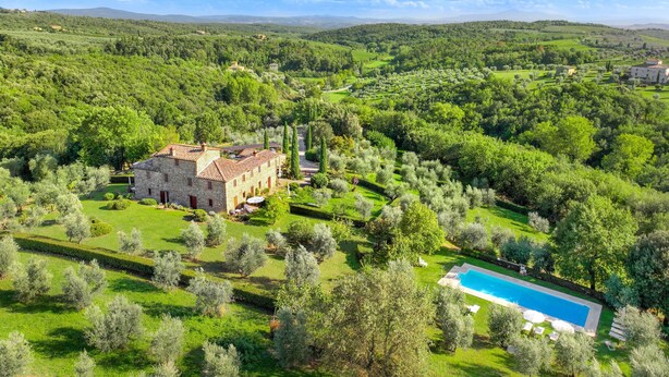 A large stone building with a swimming pool, surrounded by lush greenery and rolling hills.