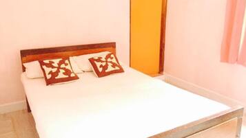 A bed with a wooden headboard and two decorative pillows, a plain wall, and a door with a yellow frame.