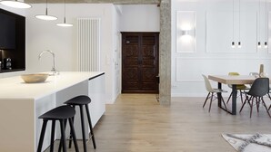 A modern kitchen with a central island, black bar stools, pendant lighting, and a dining area with a wooden table and chairs.