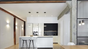 A modern kitchen with a central island, pendant lighting, and a rustic wooden beam ceiling.