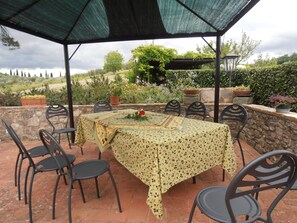 An outdoor patio with a table covered in a patterned tablecloth, surrounded by chairs.