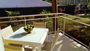 A balcony with a table and chairs, a bowl of bananas, and a view of a garden and buildings.