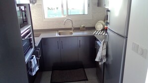 A compact kitchen with a sink, cabinets, a refrigerator, and a window.
