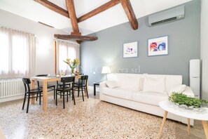 A modern living room with a dining area, white furniture, and a speckled floor.