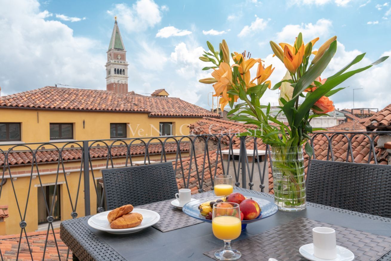 A dining table with breakfast items, a vase with flowers, and a view of a building with a tower.