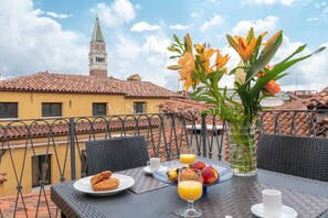 A dining table with breakfast items, a vase with flowers, and a view of a building with a tower. - Ve.N.I.Ce Cera San Marco Terrace (Venezia)