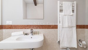 Un baño con lavamanos blanco, espejo y toallero.
