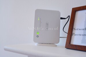 A white electronic device on a white surface with a framed picture in the background.
