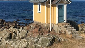 A small yellow building with a flagpole, located on rocky terrain near a body of water. - Idyllic holiday home near Örkelljunga, sun terrace, wood-burning stove, forests and lakes (Örkelljunga)