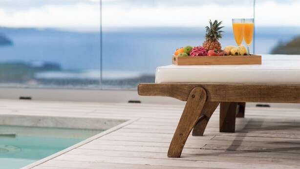 A wooden deck with a white cushioned bench, a wooden tray with fruits and a glass of orange juice, and a view of the ocean. - Plunge pool, terraces, garden, BBQ & lounge [A] (Icod de los Vinos)