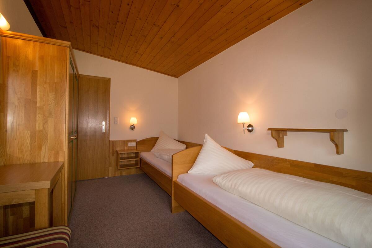 A room with two wooden beds, a wooden table, and a bench.