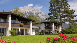 A hotel with a mountain backdrop, featuring a well-maintained lawn and blooming flowers in the foreground. - Chalets St. Wendelin (Telfs)
