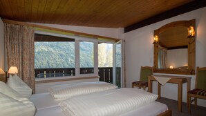 A bedroom with two beds, a wooden desk, a chair, and a large window with a mountain view. - Chalets St. Wendelin (Telfs)
