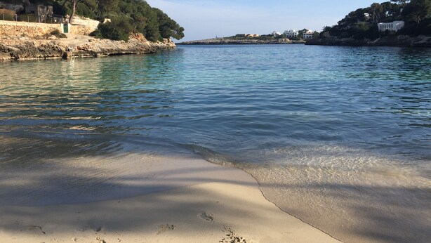 A coastal scene with clear water, sandy beach, rocky cliffs, and buildings on the hills. - House for 8 people (4 bedrooms) with swimming pool and superb view of the marina (Cala d'Or)