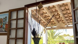 A room with a wooden table, a decorative vase with sticks, a colorful painting, and a view of greenery and buildings outside. - House for 8 people (4 bedrooms) with swimming pool and superb view of the marina (Cala d'Or)