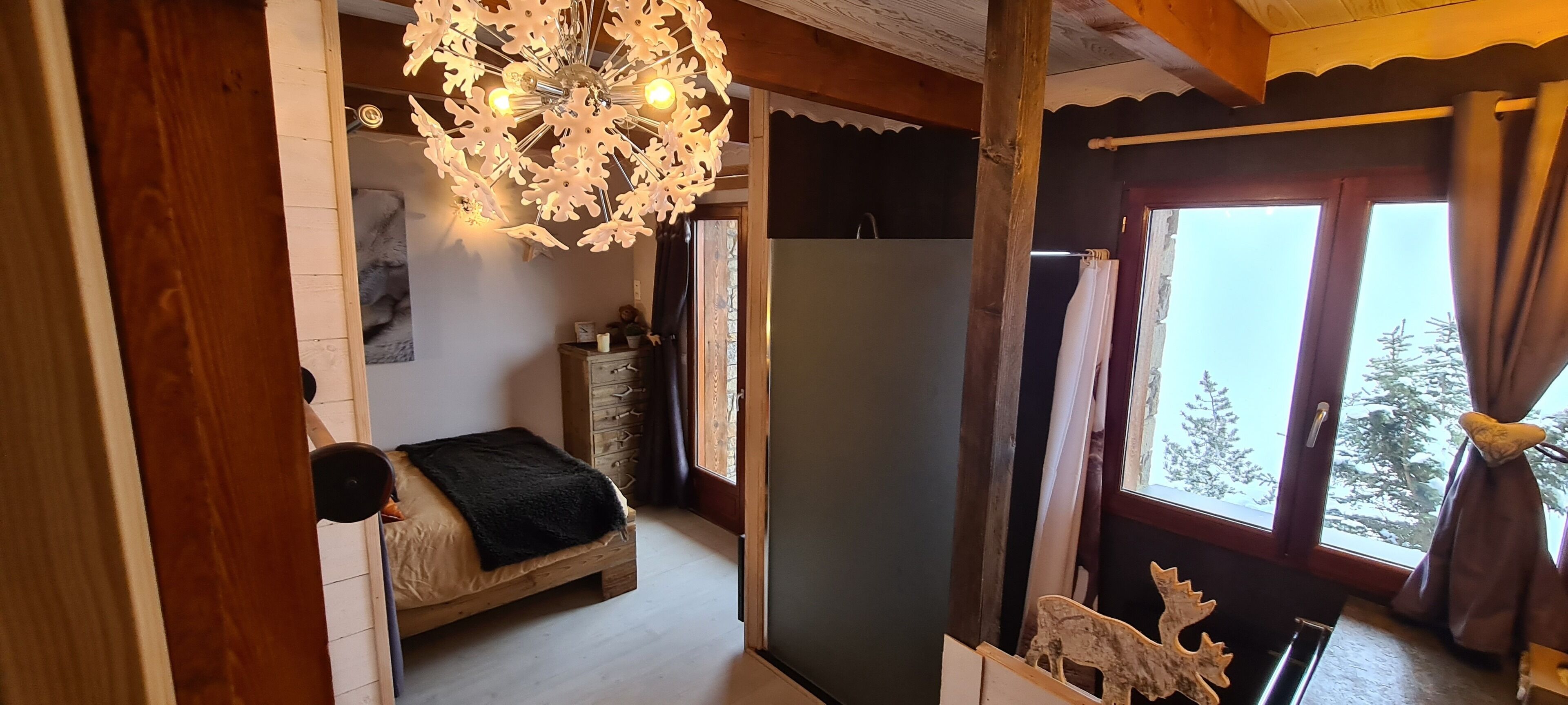A bedroom with a bed, a wooden headboard, a chandelier, a dresser, and a window with curtains.